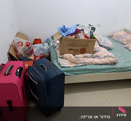 חדר עם מזוודות, קופסאות ואריזות על המיטה